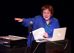 Woman with computer and mixing board holding a paper and pointing.